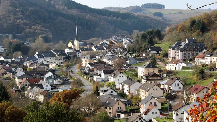 Ein malerisches Dorf mit hübschen Häusern und einer Kirche. Die umliegende Landschaft ist grün und sanft geschwungen.