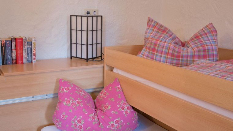 Ein gemütliches Schlafzimmer mit zwei Betten und bunten Kissen. Auf einem Nachttisch steht eine Lampe und einige Bücher sind sichtbar.