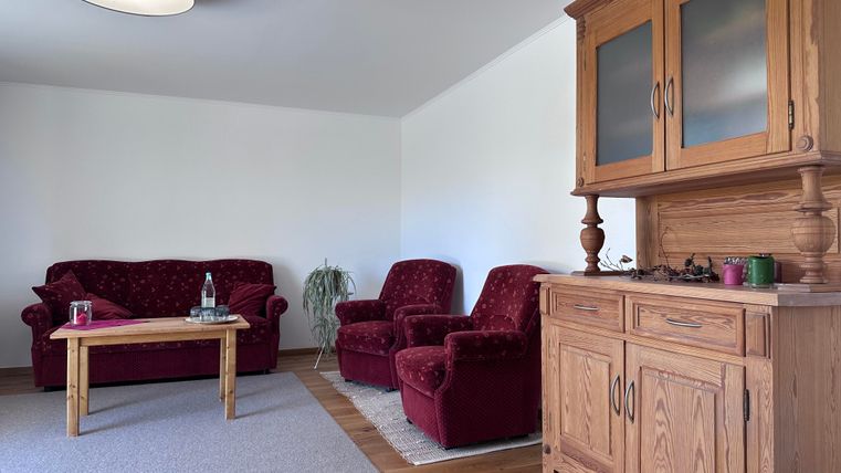 A cozy living space with red sofa and armchair groups. A wooden piece of furniture is against the wall, along with a small table and a carpet on the floor.