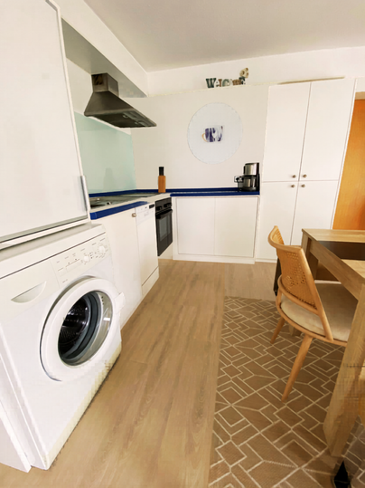 Een moderne keuken met een wasmachine, een fornuis en een eettafel. De vloer heeft een aantrekkelijk patroon en de muren zijn licht.