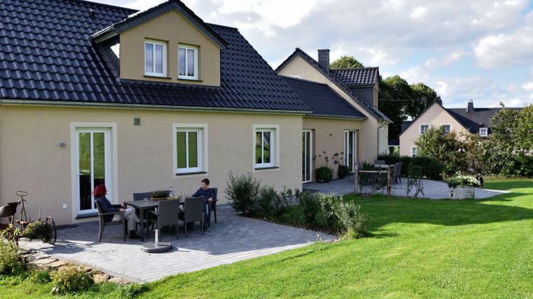 Ein modernes Haus mit einem gepflegten Garten. Im Vordergrund stehen Sitzmöbel auf der Terrasse.