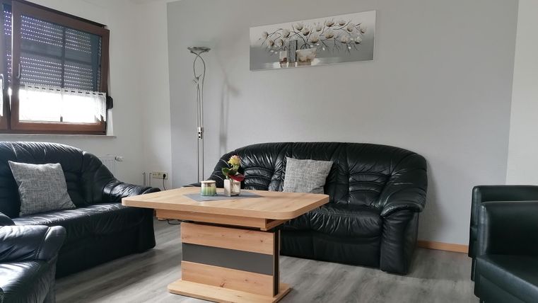 Un salon confortable avec des meubles en cuir noirs et une table basse en bois. Un tableau décoratif est accroché au mur, et une lampe sur pied fournit un éclairage supplémentaire.