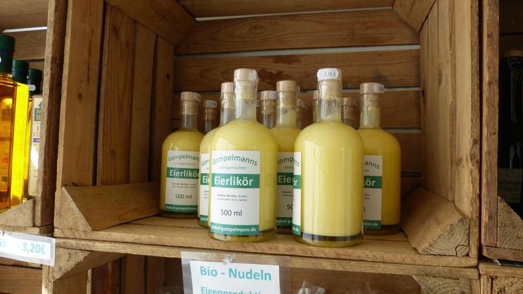 Bottles of egg liqueur are on a wooden shelf. The bottles are yellowish and labeled.
