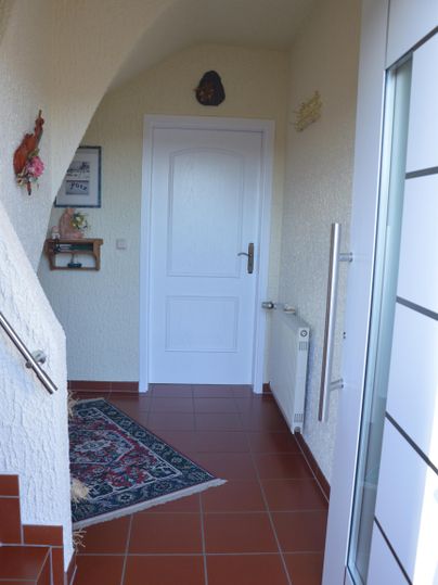 Ein heller Eingangsbereich mit einem Teppich und einer weißen Tür. Die Wände sind in neutralen Farben gehalten, und eine Treppe führt nach oben.