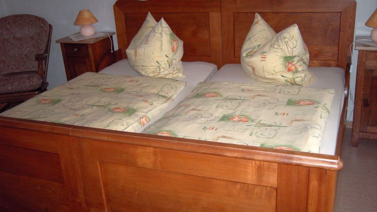 Ein gemütliches Schlafzimmer mit einem Holzbett und zwei Kopfkissen. Neben dem Bett steht ein Nachttisch mit einer Lampe.