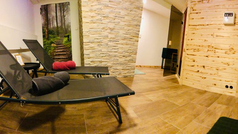 Une zone de détente calme avec deux chaises longues et un mur en pierre. En arrière-plan, on peut voir une image d'un chemin forestier.