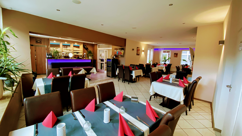 Ein einladendes Restaurant mit eleganter Einrichtung. Die Tische sind mit weißen Tischdecken und roten Servietten gedeckt.