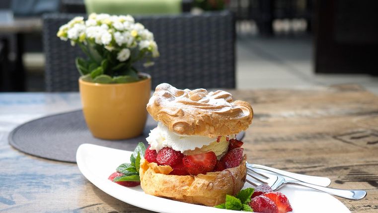 Ein köstliches Dessert mit frischen Erdbeeren, Sahne und einem knusprigen Waffelboden auf einem weißen Teller. Im Hintergrund steht ein Topf mit blühenden Pflanzen.