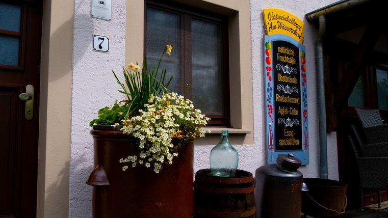 Ein charmantes Haus mit einem Fenster und einer farbenfrohen Tafel. Vor der Tür steht ein Blumentopf mit blühenden Pflanzen.