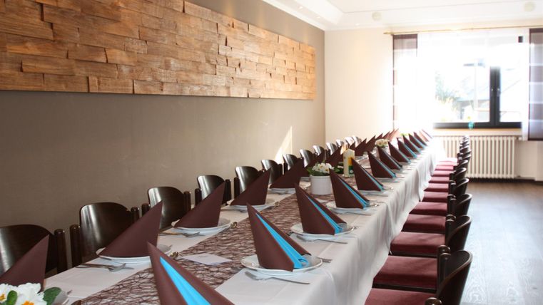 Ein eleganter Esszimmer mit einem langen Tisch, der für eine Veranstaltung gedeckt ist. Die Tischdecken sind dekoriert mit braunen und blauen Servietten und eine Holzwand sorgt für eine angenehme Atmosphäre.