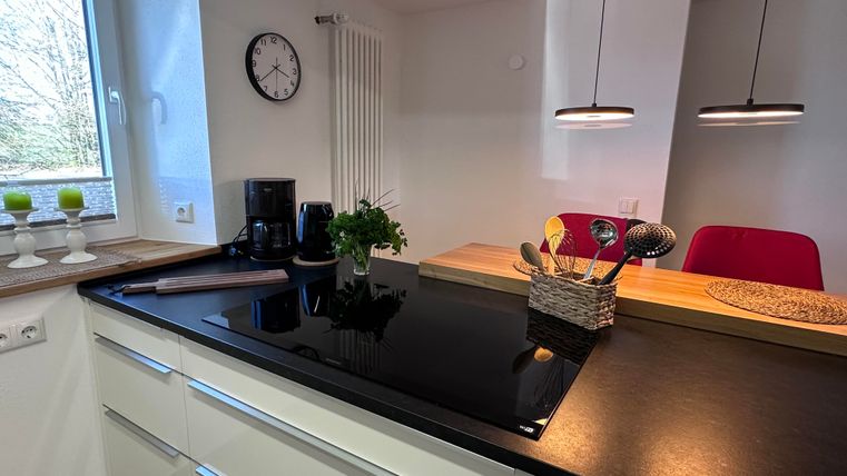 A modern kitchen with a black countertop and minimalist white cabinets. In the background, windows and decorative elements are visible.