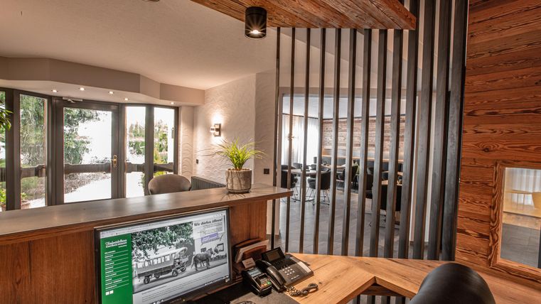 Ein moderner Empfangsbereich mit holzverkleidetem Design. Durch die großen Fenster ist viel Tageslicht zu sehen, und im Hintergrund befinden sich weitere Sitzbereiche.