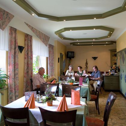 Ein gemütliches Restaurant mit gedeckten Tischen und einer einladenden Atmosphäre. Einige Gäste sitzen zusammen und genießen ihre Zeit.