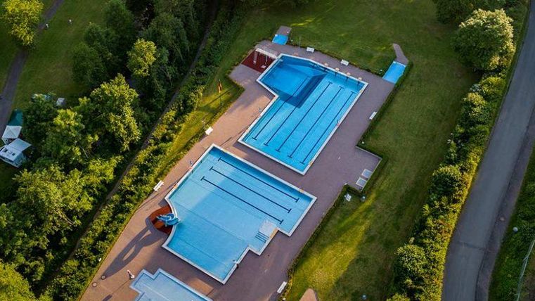 Ein weitläufiges Schwimmbad mit mehreren Becken, umgeben von grünen Bäumen. Die blauen Wasserflächen strahlen Ruhe und Entspannung aus.
