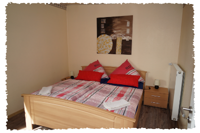 Ein gemütliches Schlafzimmer mit einem großen Bett und bunten Kissen. An der Wand hängt ein modernes Kunstwerk, und die Möbel sind aus hellem Holz.