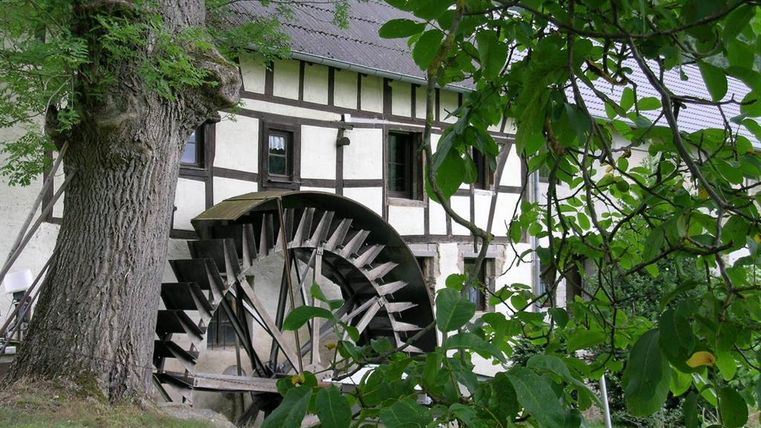 Fachwerkhaus mit Wasserrad, umgeben von Bäumen.