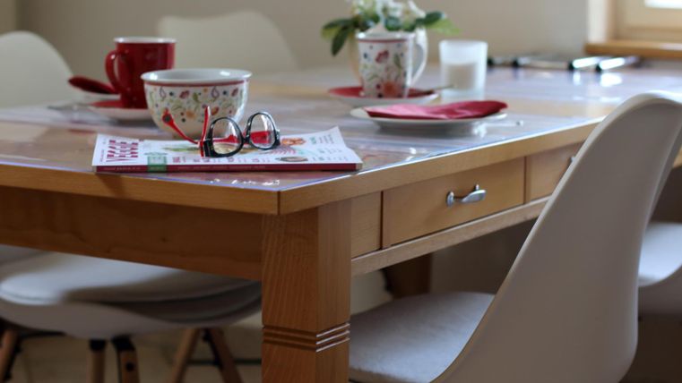 Ein gemütlicher Esstisch aus Holz mit einer eleganten Tischdecke. Auf dem Tisch stehen Tassen, eine Schüssel und eine kleine Pflanze.