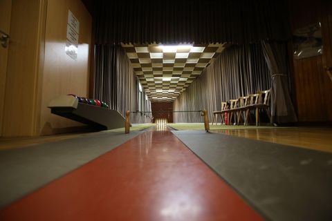 A bowling alley with a long wooden lane and colorful pins on the side. The walls are decorated with curtains and the ceiling has a checkerboard design.