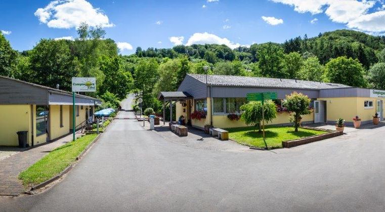 Eine malerische Anlage mit gelben Gebäuden umgeben von grüner Natur. Der klaren Himmel und die Bäume verleihen der Umgebung eine einladende Atmosphäre.