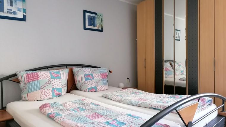 Une chambre confortable avec un lit double et des couettes colorées. Des images sont accrochées au mur, et un grand miroir armoire se trouve à côté.