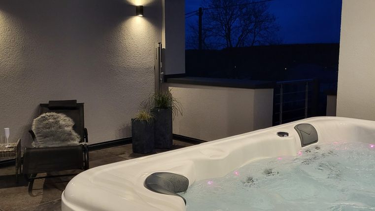 Ein Whirlpool auf einer modernen Terrasse bei Nacht. Sanftes Licht und eine entspannte Atmosphäre schaffen eine einladende Umgebung.