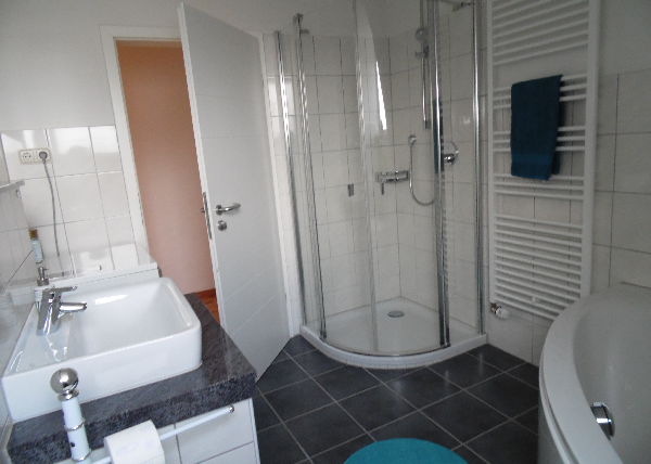 Ein modernes Badezimmer mit einer Dusche und einer Badewanne. Die Wände sind gefliest und die Einrichtung ist schlicht und elegant.