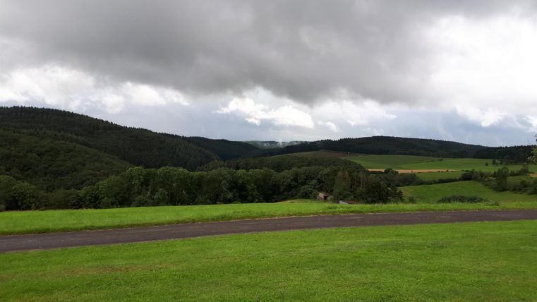 Eine grüne Landschaft mit sanften Hügeln und bewölktem Himmel. Der Bereich wirkt ruhig und einladend.