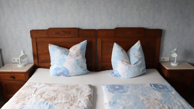 Ein gemütliches Schlafzimmer mit einem großen Bett und dekorativen Kissen. Die Wände sind hellblau gestrichen und das Mobiliar ist aus dunklem Holz.