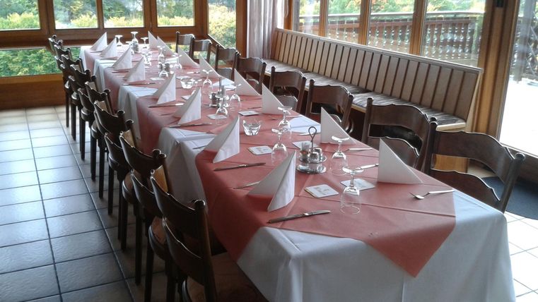 A nicely set table in a restaurant with a window view. The table is decorated with white and red tablecloths, as well as dishes and glasses.