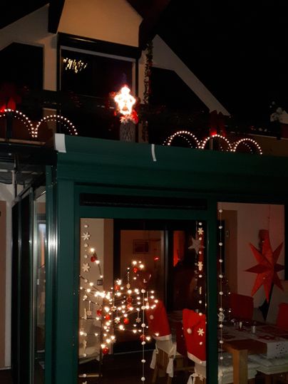 Ein festlich dekoriertes Haus mit Lichtern und Weihnachtssternen. Der Abendhimmel sorgt für eine gemütliche Atmosphäre.