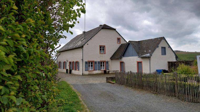 Ein charmantes, ländliches Haus mit grauem Dach und bunten Fensterläden. Der Weg führt zu dem Haus, umgeben von Bäumen und einem kleinen Garten.