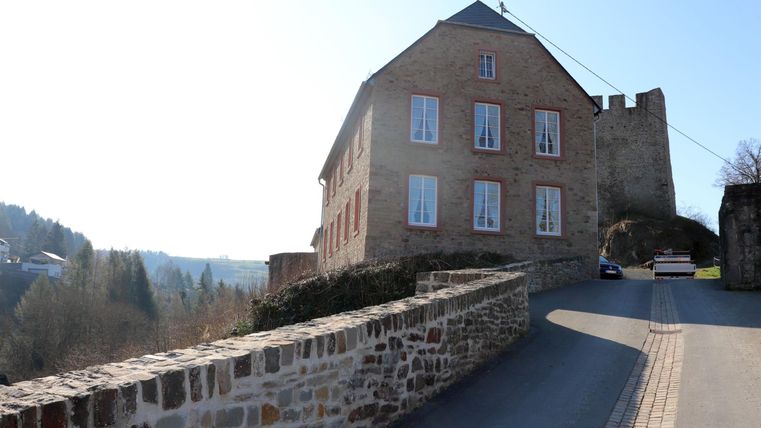 An old stone building with shutters and a historical character. The street gently passes by the facade.