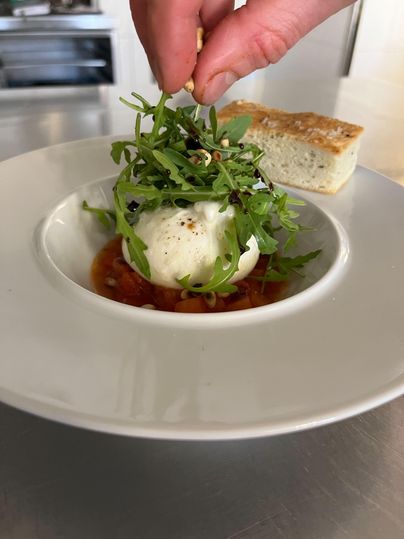 Ein Teller mit frischer Burrata in einer Tomatensauce, garniert mit grünen Blättern. Daneben liegt ein Stück Brot.