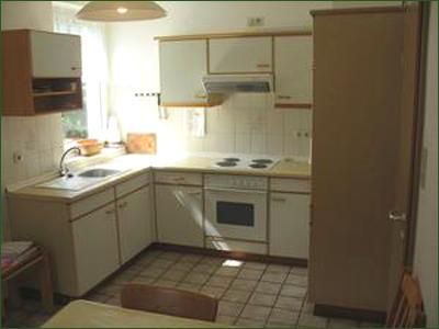 Eine helle Küche mit weißen Schränken und Kochgeräten. Der Raum hat eine gemütliche Atmosphäre und bietet einen Essplatz.