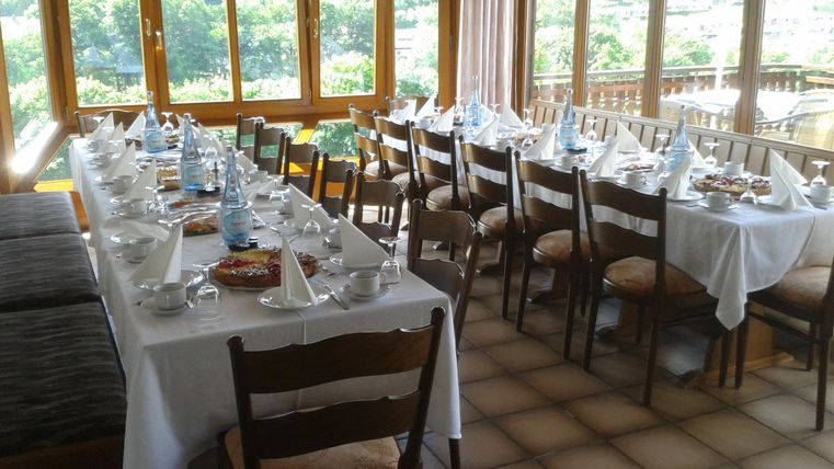 An elegant dining area with white-covered tables and wooden chairs. Large windows offer a view of the surrounding landscape.