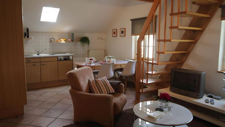 Eine gemütliche Wohnung mit einer offenen Küche, einem Tisch und modernen Möbeln. Eine Treppe führt zu einem oberen Bereich, und große Fenster sorgen für viel Tageslicht.