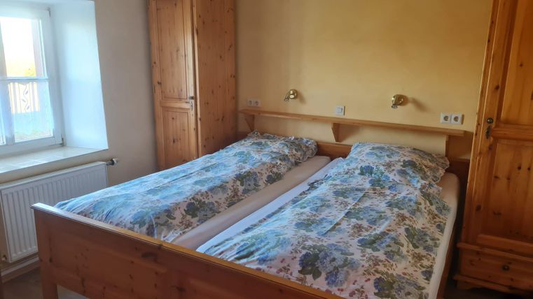 Ein gemütliches Schlafzimmer mit zwei Betten und Holzmöbeln. Die Wände sind in warmen Gelbtönen gestrichen und ein Fenster lässt Tageslicht herein.